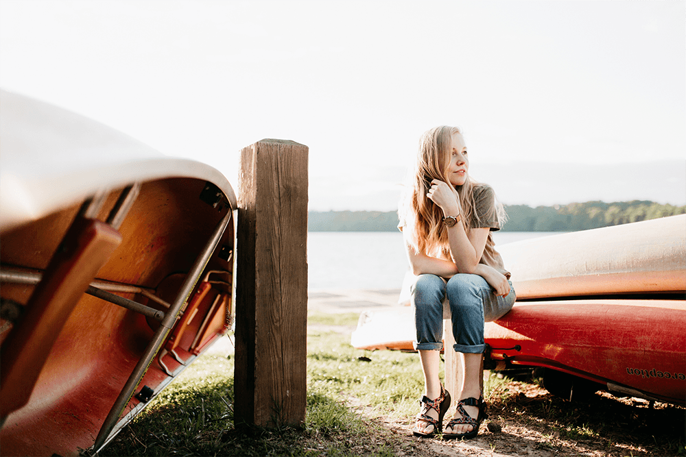 Young expat woman sitting on a canoe on a lake shore