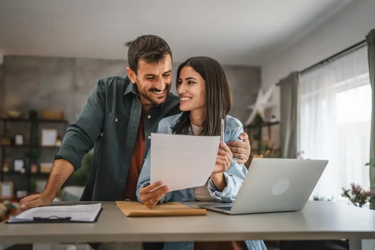 Couple smiling while reviewing a document together at a home desk with a laptop and folder, comparing expat tax professionals.