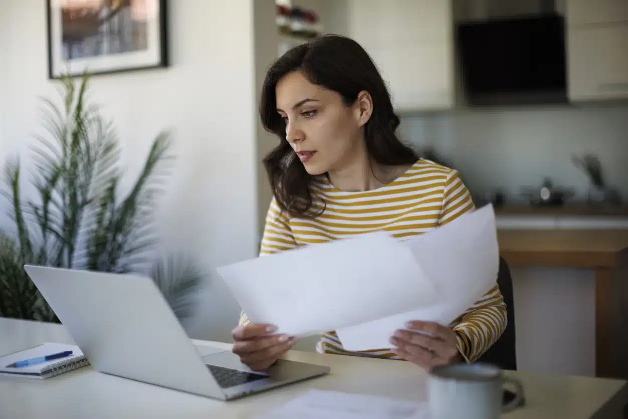 woman reviewing financial documents while working on laptop at home