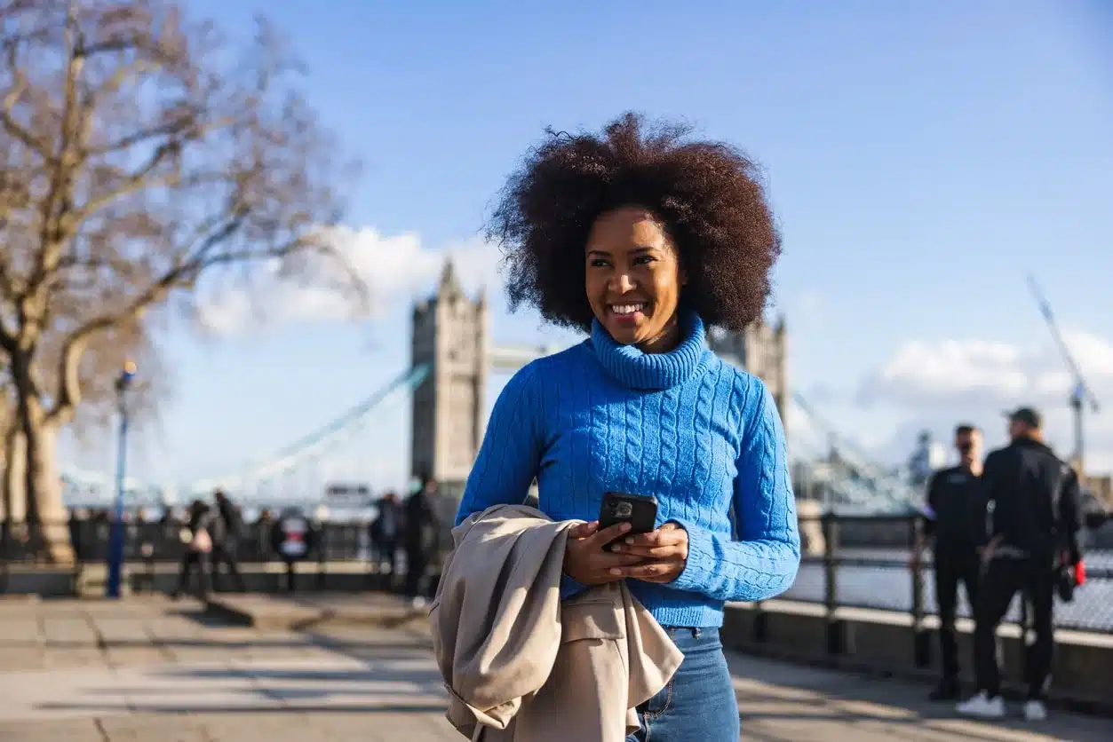 A happy black adult female exploring London alone on a beautiful sunny day. She is looking around and admiring the beautiful landmarks of London.