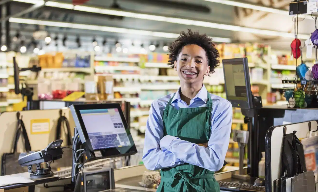 teenage retail worker standing at checkout counter in store representing minors earning income and tax obligations