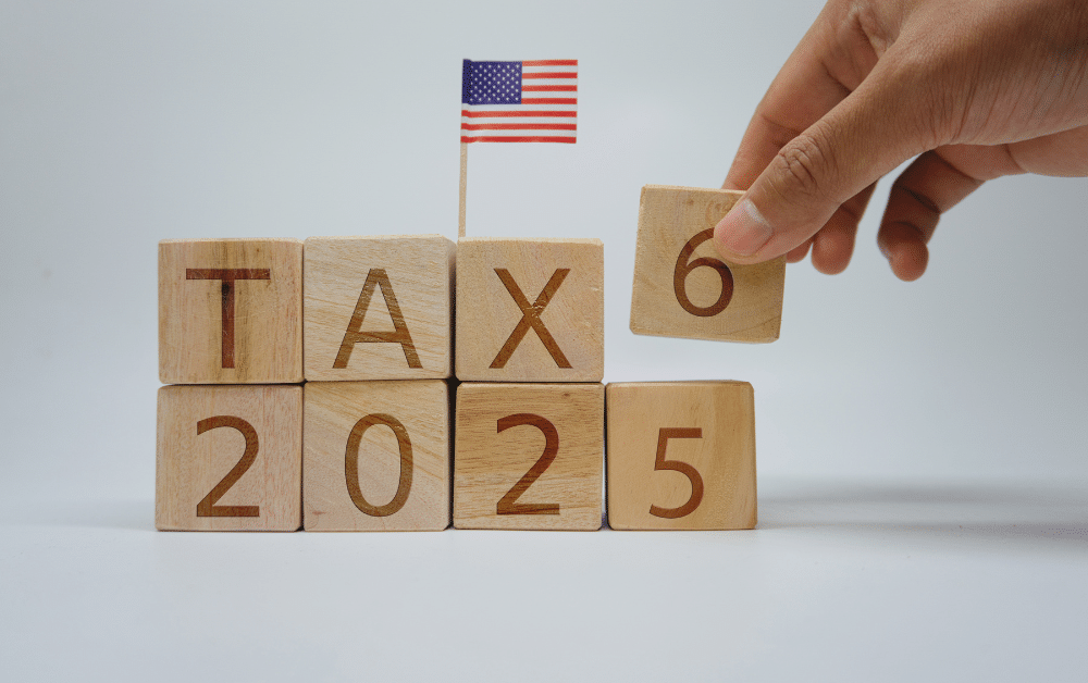 Hand changing wooden blocks from TAX 2025 to TAX 2026 with American flag, representing IRS tax year transition