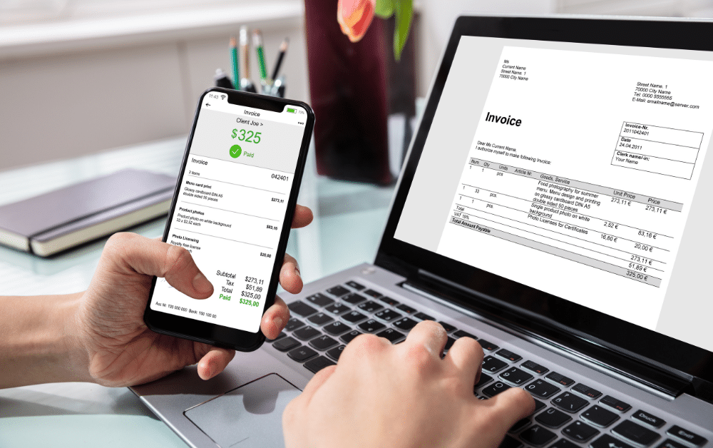 A person reviews invoices on both a smartphone and a laptop, representing how U.S. expats manage cross-border billing, payments, and currency conversions for international clients.