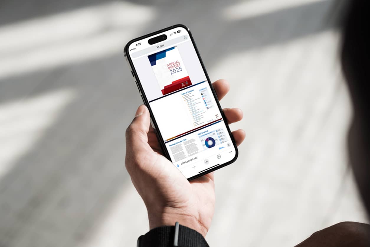 A person holding a smartphone displaying the IRS Criminal Investigation Annual Report 2025.