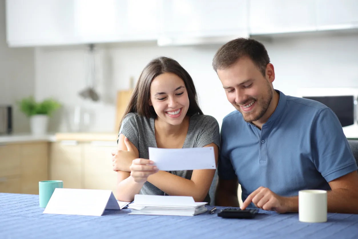 Happy couple opening a letter at home, celebrating a larger IRS refund this tax season.