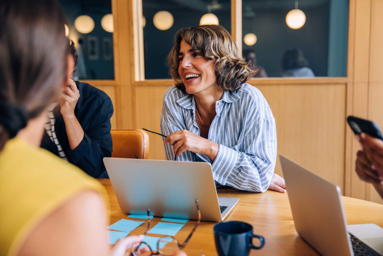 Business owner laughing with colleagues around a meeting table, laptops and notes in front of them.